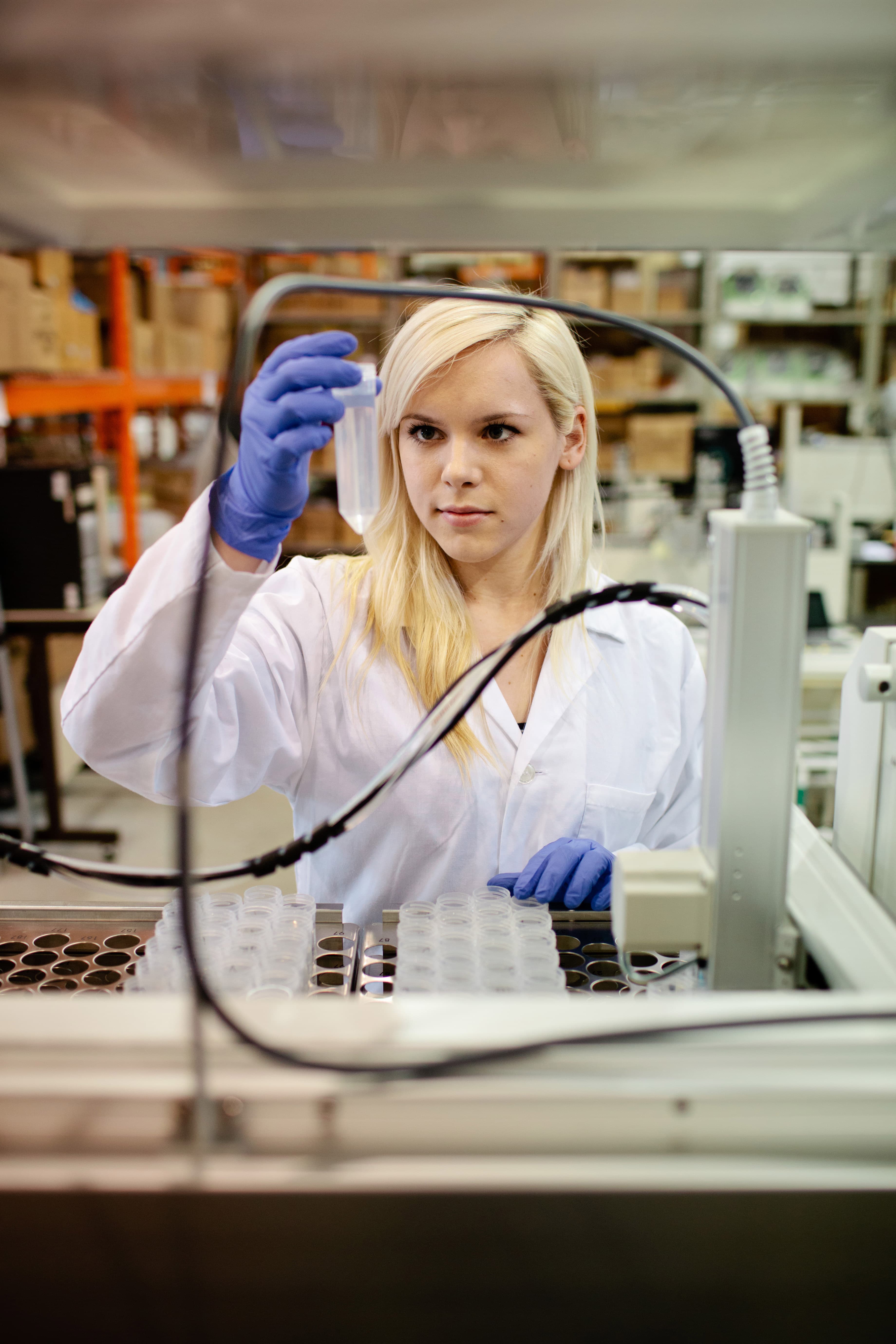 person in lab coat and gloves examines liquid