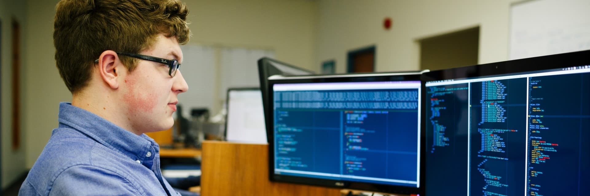 Person looks at two computer screens, with code on them.