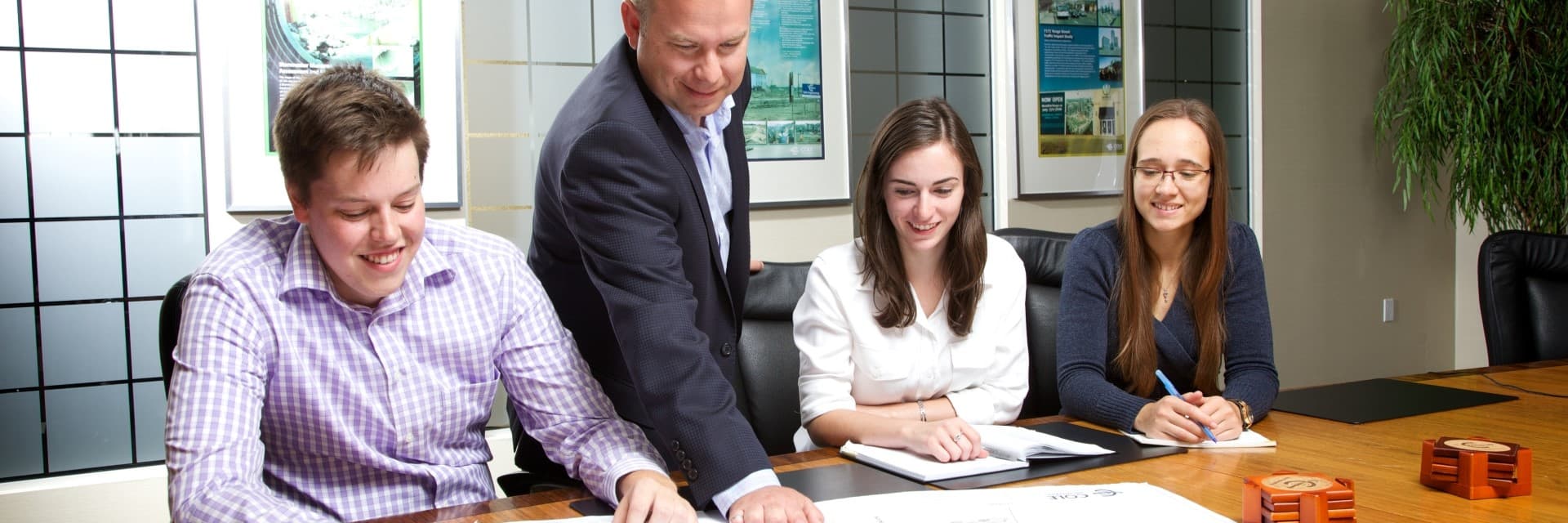 Three co-op students sit at a table, while employer points out something on a document.
