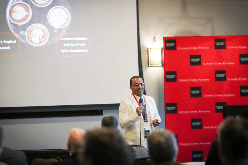 Dr. Ali Dehghantanha speaking at the launch of the CCF. He holds a microphone speaking to an audience with a slideshow and banner in the background.